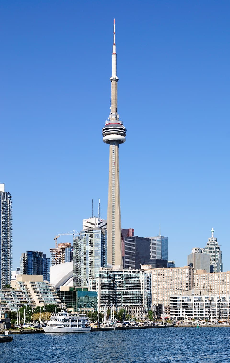 The CN Tower rises above the Toronto skyline and waterfront under a clear blue sky.